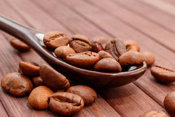 Grains of coffee close-up. Coffee beans are located on a spoon among the wooden texture. Coffee grains are located on a spoon on a wooden. Java composition from whole grains of coffee.
