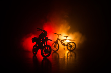 Plakat Silhouette of motorcycle and bicycle on a dark cloudy toned background. A silhouette of a motorcycle and bike from a side view. Selective focus