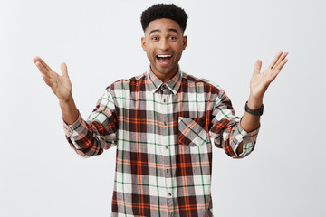 Naklejka premium Positive emotions. Isolated portrait of young happy tan-skinned guy with afro haircut in long-sleeved checkered shirt spreading hands, being excited to see old friend after vacation.