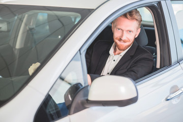Happy man buying new car in auto showroom. Smiling man sitting in new car.