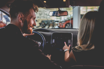Man and woman sitting on front seats of new car. Happy couple in auto showroom choosing new vehicle.