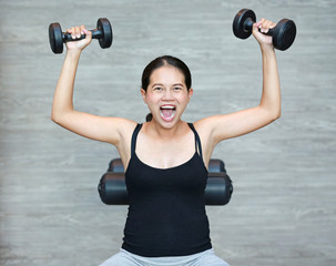Fototapeta na wymiar Excited woman holding dumbbells in sports hall.