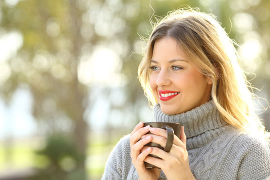 Woman thinking holding a cup of coffee in winter