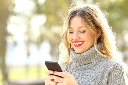 Happy Woman Reading Text On Phone In Winter