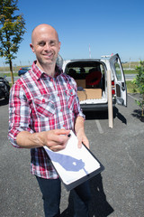 delivery driver smiling at camera next to his van