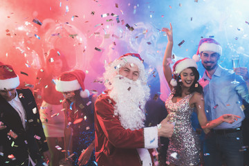 A man dressed as Santa Claus has fun at a New Year party. Together with him have fun friends.