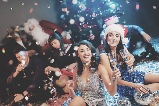 Two girls are sitting on the floor. Around them is scattered confetti. They rest after the party for the new year