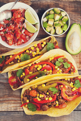 Three Mexican tacos with minced beef and mix vegetables on old rustic table. Mexican dish with sauces salsa in bowl and avocado. Spicy and hot street food. Top view