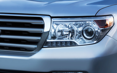 Blue toned close up photo of a car headlight with grille.