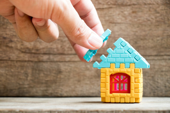 Man hold piece of puzzle to complete the home model object on wood background (Concept of dream home, mortgage investment, family fulfillment)