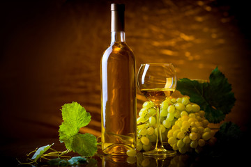 Wine. Bottle and a glass of white wine with ripe grapes still life. White wine on a gold background. Christmas wine
