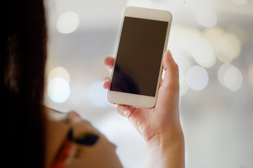 Mock up smartphone blank screen in female hands in blurred office interior background.