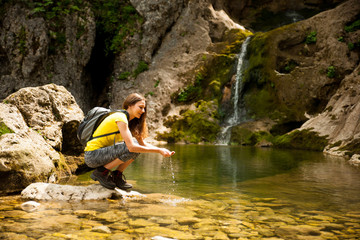Fototapeta na wymiar active young woman drinking water from a mountain creek on a warm spring day