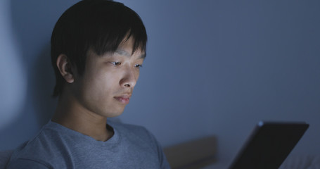 Asian man watching on tablet on bed