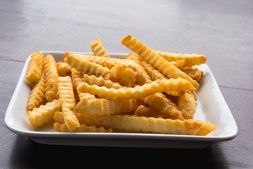French fries in a white plate on a wooden table.