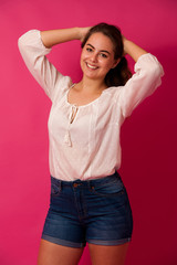 Cute young woman in light summer clothes over pink background