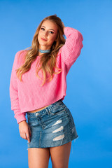 Beautiful funky woman in pink sweater and jeans skirt dance over blue background