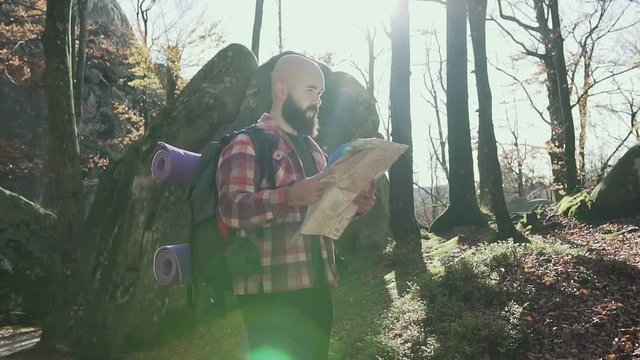 Stylish hipster man traveler with backpack holding map and exploring on top of mountains, travel concept. Autumn. A handsoome man wearing a beard keeps a tourist map in his hands