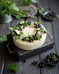 A modern mousse cake with a crusty nut layer, a layer of black wild currant and a mousse of white chocolate and yogurt. The cake is decorated with fresh currant berries and leaves of white chocolate