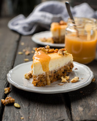 Carrot nut vanilla cheesecake with salty homemade caramel on a white plate on a dark wooden vintage background. Two pieces of homemade cheesecake. Caramel sauce in a jar.