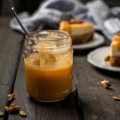 Caramel sauce in a jar. Carrot nut vanilla cheesecake with salty homemade caramel on a white plate on a dark wooden vintage background. Two pieces of homemade cheesecake. 