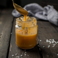 Caramel sauce in a jar. Carrot nut vanilla cheesecake with salty homemade caramel on a white plate on a dark wooden vintage background. Two pieces of homemade cheesecake. 