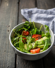Useful tasty salad with arugula, fresh strawberries and avocado, seasoned with honey, wine vinegar, olive oil and poppy seeds on a vintage dark vintage background.