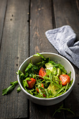 Useful tasty salad with arugula, fresh strawberries and avocado, seasoned with honey, wine vinegar, olive oil and poppy seeds on a vintage dark vintage background.