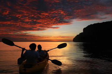 Mother and daughter kayaking in the ocean with red sky sunset