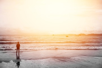 Silhouette of a girl standing on the beach with the sunset light and copy space for your design