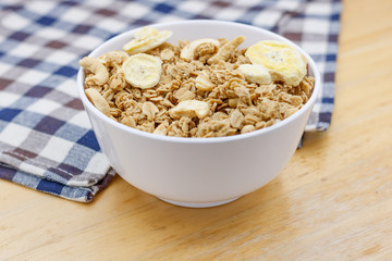 Healthy breakfast, granola with nuts and dry bananas in white blow on wooden table with wooden spoon and cute fabric.