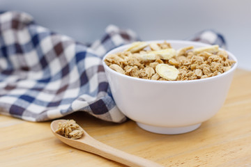 Healthy breakfast, granola with nuts and dry bananas in white blow on wooden table with wooden spoon and cute fabric.