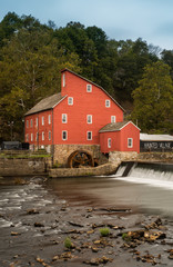 The historic Red Mill in Clinton NJ with people fishing in the river. The village also decorated...