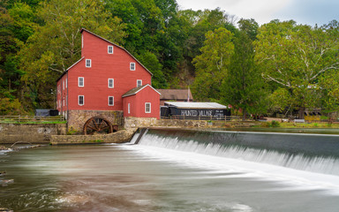 The historic Red Mill in Clinton NJ with people fishing in the river. The village also decorated...