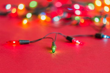 Xmas lights bulbs on string (selective focus) in blue, yellow, green, pink & red colours; on vivid red velvet background with copy space & bokeh (blur light) for Christmas tree, new year celebration