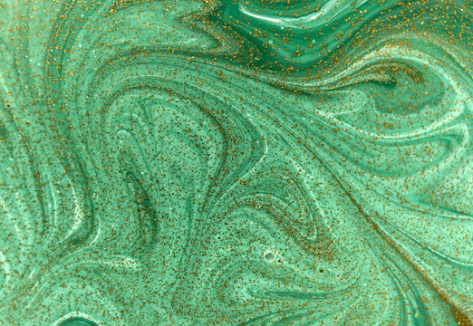 Marbled green abstract background with golden sequins. Liquid marble ink pattern.