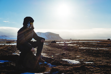 Young traveler man sitting on the rock under bright sun in the morning
