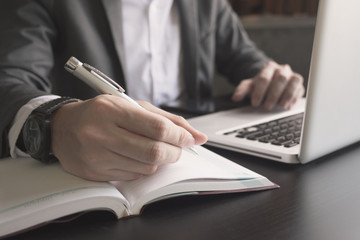 Close up of businessman writing note and using a laptop on the office desk.