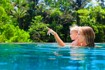 Happy family - mother, baby son learn to swim. Joyful kid has fun in luxury resort swimming pool. Travel lifestyle at summer beach vacation, children water sports activity, swimming lesson with parent