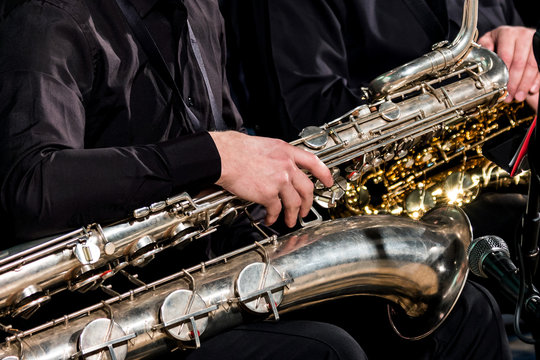 A saxophonist man put a baritone saxophone on his knees and waits for the orchestra's performances.