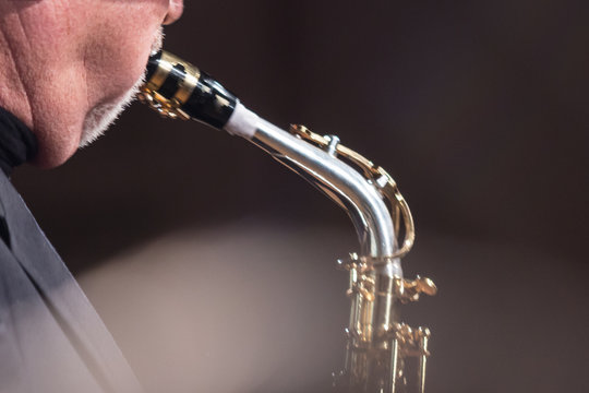 Elderly saxophonist with a second chin, blowing into a saxophone. Blured picture.