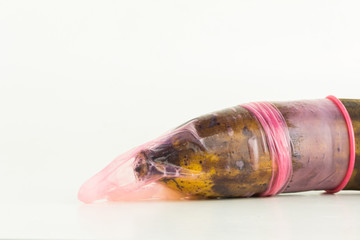 close up color pink used condom with sperm cover old banana, isolated on white background.
