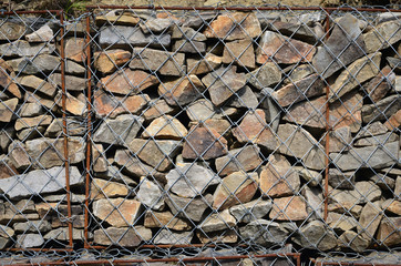 Photo of several gabions. The mesh cells of the cubic form are filled with mountain stones of...