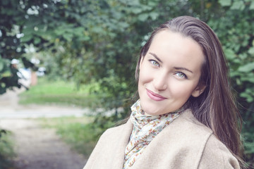 Naklejka premium Smiling woman with a perfect smile, walking in the coat in autumn Park and looking at camera.