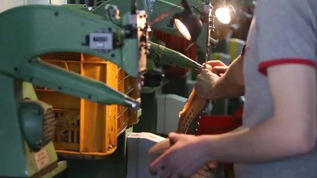 Slow motion of shoemaker making sole of shoe on machine in workshop.