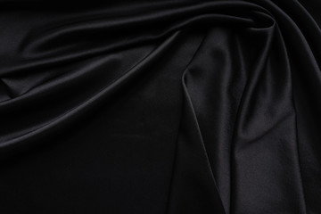 Dark black silky, satin  fabric, wave, draperies. Beautiful textile backdrop. Close-up. Top view 