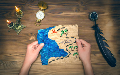 Treasure map and compass on wooden table. Treasure hunt background. Adventurer man holding in hands...