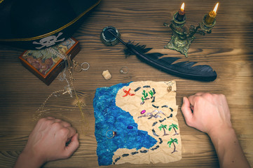 Crumpled treasure map and pirate hat on wooden table. Treasure hunt. Pirate man learing treasure map where buried gold chest marked on the map.