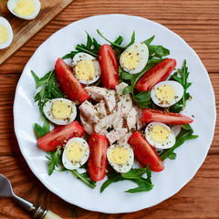 Fresh vegetable salad with chicken breast and quail eggs. Salad with tomatoes, rucola, quail eggs, chicken breast and spices on a plate and a wooden background. Healthy nutrition. Closeup. Top view