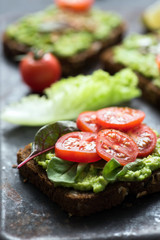 Toast with avocado, spinach and cherry tomato on whole grain rye bread. Closeup view, selective focus
